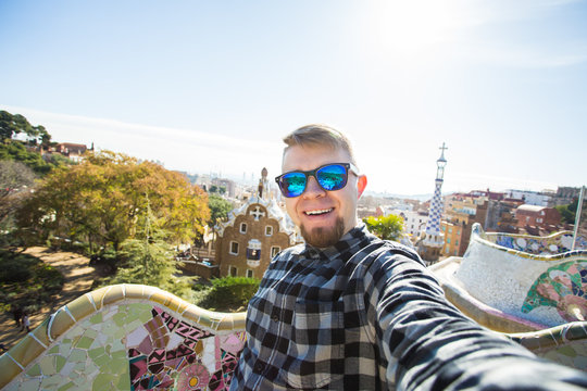 Travel and holidays concept - Handsome man looking at camera taking photo with smart phone smiling in Park Guell, Barcelona, Spain.