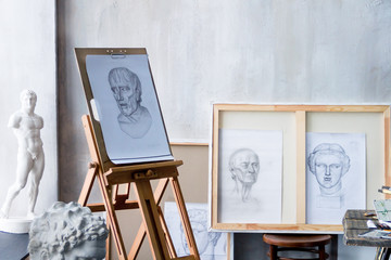 Modern freelancer artist sculptor creator art workshop workplace studio exhibition interior with pencil drawings on wooden esasel, sketches: male portrait and gypsum plaster sculptures in university