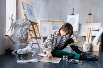 Modern young freelancer artist sculptor woman female creates new art masterpiece drawing sketch at art workshop workplace studio exhibition with drawings, sketches and gypsum plaster sculptures. © Monstar Studio