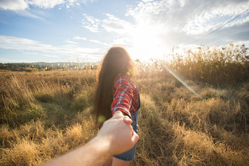 Traveling together. Follow me. Young woman holding boyfriend's hand walking in the field on sunset