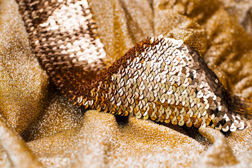 Gold fabric background. On the background lies a golden belt with scales like fish has and shines