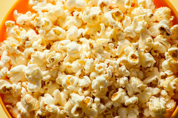 An orange bowl with popcorn isolated on yellow background