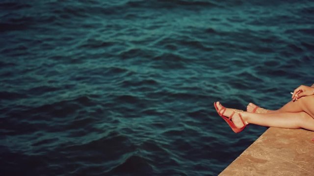 woman in red sandals sitting on a pier smoking a cigarette