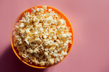 An orange bowl with popcorn isolated on pink background