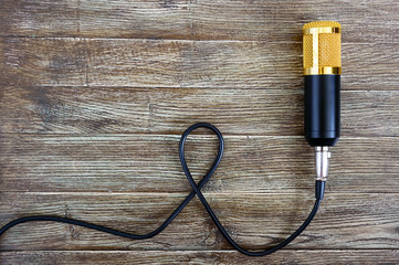 Condenser gold microphone with cable lies on a wooden table with copy space. Musical theme. Flat lay. Top view.