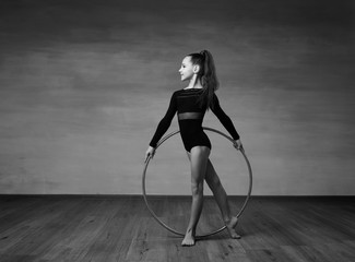 Black and white photo, a girl gymnast in a black bathing suit looks in profile in the hands of a gymnastic hoop.