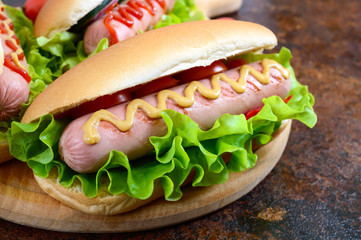 Delicious hot dogs with sausage grill, ketchup, mustard, lettuce, tomatoes on a wooden tray. Close up