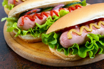 Delicious hot dogs with sausage grill, ketchup, mustard, lettuce, tomatoes on a wooden tray. Close up