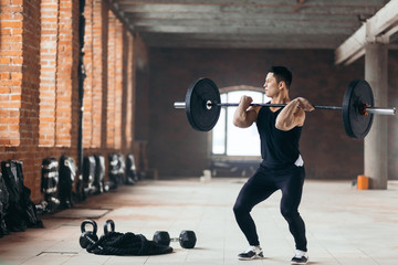 Handsome man doing squats with barbell in the sport center. guy is fond of professional sport. full...