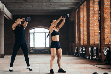 Obraz premium man and woman throwing weight in the sport center. full length photo. kettlebell lifting. flexibility training