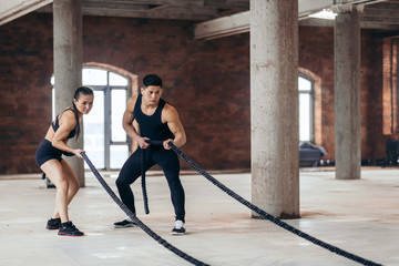 serious guy and girl pulling battle ropes at gym, health and body care, copy space, wellness