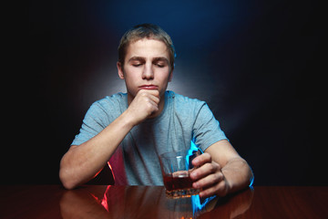 Portrait of a man looking at a glass of whiskey in his hand. Man in a gray t-shirt posing in the studio with a glass of alcohol in his hand