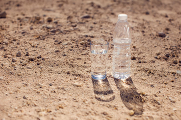 Glass and bottle of water in the desert. Thirsty, heat and drought concept