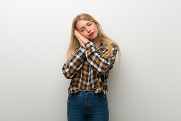 Blonde young girl over white wall making sleep gesture in dorable expression