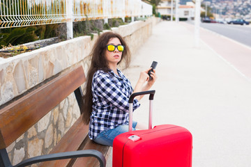 Obraz premium Technology, travelling and people concept - young woman sit on bench in sunny glasses and typing on phone