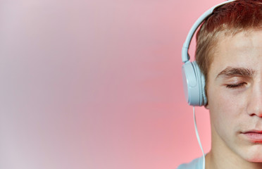 Portrait of a young guy close up who listens to music in headphones white with closed eyes on a red background