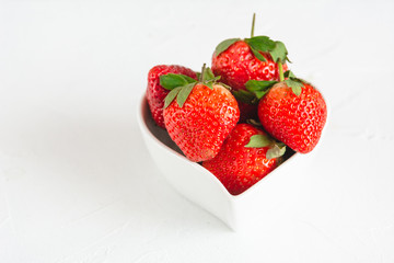 Fresh strawberries in a heart shaped bowl isolated on white background.