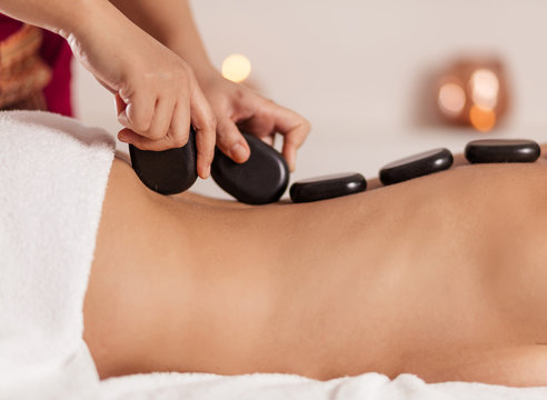 masseur putting black stones on the clien's back. relieving stress and pain. close up side view photo.
