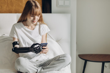 happy girl with artificial arm sending messages, sms while resting at home. happiness, free time,...