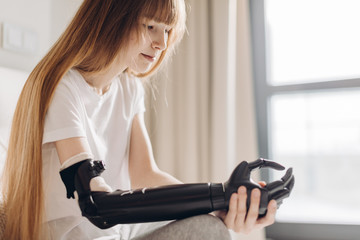 pensive serious girl having a cyber arm sitting in the light room . close up photo. young woman...