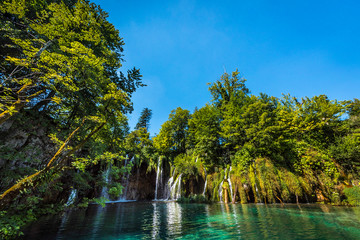 Sun-drenched deciduous forest with waterfalls and turquoise lake, Plitvice lakes, Croatia