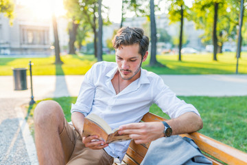 Smiling student reading a book in the park, studying and preparing for exams at the university or college. Technology, communication, education and remote working concept, copy space