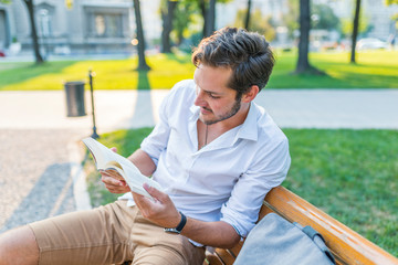 Smiling student reading a book in the park, studying and preparing for exams at the university or...