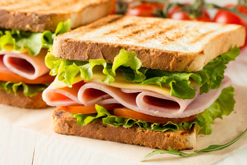 Close-up photo of a club sandwich. Sandwich with meat, prosciutto, salami, salad, vegetables, lettuce, tomato, onion and mustard on a fresh sliced rye bread on wooden background. Olives background.