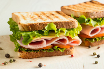 Close-up photo of a club sandwich. Sandwich with meat, prosciutto, salami, salad, vegetables, lettuce, tomato, onion and mustard on a fresh sliced rye bread on wooden background. Olives background.