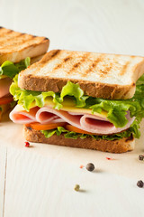 Close-up photo of a club sandwich. Sandwich with meat, prosciutto, salami, salad, vegetables, lettuce, tomato, onion and mustard on a fresh sliced rye bread on wooden background. Olives background.