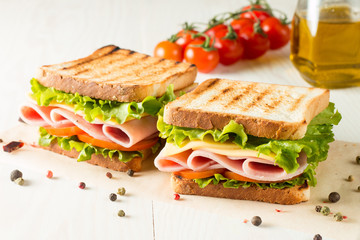 Close-up photo of a club sandwich. Sandwich with meat, prosciutto, salami, salad, vegetables, lettuce, tomato, onion and mustard on a fresh sliced rye bread on wooden background. Olives background.
