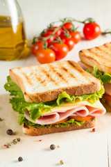 Close-up photo of a club sandwich. Sandwich with meat, prosciutto, salami, salad, vegetables, lettuce, tomato, onion and mustard on a fresh sliced rye bread on wooden background. Olives background.