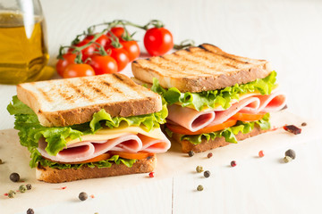 Fototapeta Close-up photo of a club sandwich. Sandwich with meat, prosciutto, salami, salad, vegetables, lettuce, tomato, onion and mustard on a fresh sliced rye bread on wooden background. Olives background. obraz