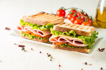 Close-up photo of a club sandwich. Sandwich with meat, prosciutto, salami, salad, vegetables, lettuce, tomato, onion and mustard on a fresh sliced rye bread on wooden background. Olives background.