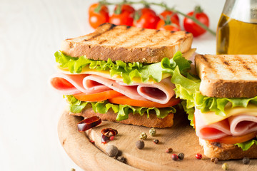 Close-up photo of a club sandwich. Sandwich with meat, prosciutto, salami, salad, vegetables, lettuce, tomato, onion and mustard on a fresh sliced rye bread on wooden background. Olives background.