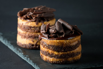 Chocolate cakes on black slatter board with mint, coffee beans on dark background, closeup photo. Fresh, tasty dessert food concept. 