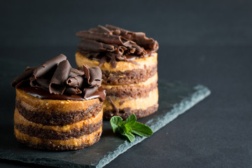 Chocolate cakes on black slatter board with mint, coffee beans on dark background, closeup photo. Fresh, tasty dessert food concept. 