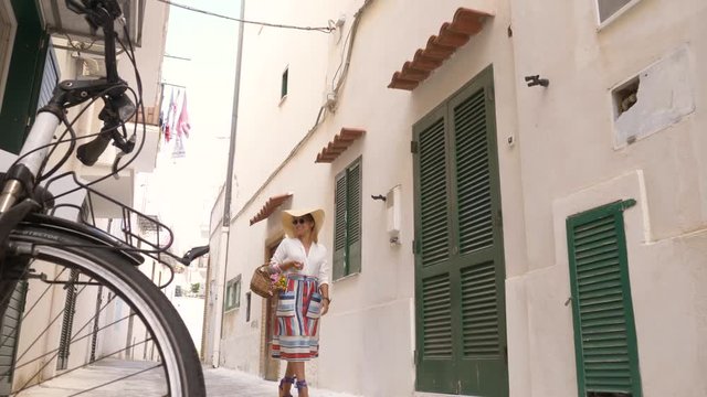Young woman walking along alley in Ponza town island, Italy. Fashion colorful dress skirt, sunglasses, flower basket.