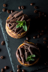 Chocolate cakes on black slatter board with mint, coffee beans on dark background, closeup photo. Fresh, tasty dessert food concept. 