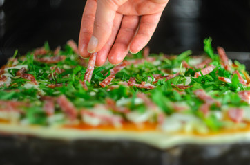 Process of making pizza. Italian pepperoni pizza with mushrooms, ruccola, tomatoes, mozzarella, garlic and sauce. Chef adds ingredients to pizza