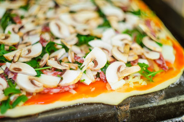 Process of making pizza. Italian pepperoni pizza with mushrooms, ruccola, tomatoes, mozzarella, garlic and sauce