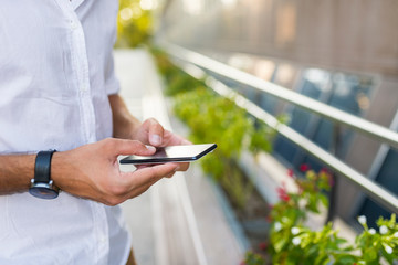 Side view shot of young smiling man using smartphone at  city street, bokeh lights, hipster guy chatting with friends at social networks via cellphone outdoor, visual effects