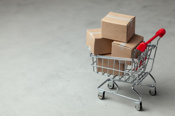 Buying goods in the online store. Cardboard boxes in the shopping basket on gray background.