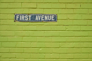 Fototapeta na wymiar Vintage First Avenue street sign, on a green painted brick wall. Sign is old and shows major sign of wear and some rust