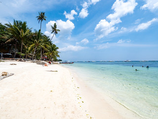 Fototapeta na wymiar Beautiful tropical beach background from Alona Beach at Panglao Bohol island with beach chairs on the white sand beach with cloudy blue sky and palm trees. Travel Vacation, november 2018