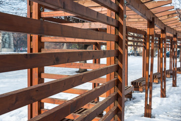 Wooden fence and benches on a small citys park at wintertime.