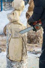 Carving sawing out a wooden sculpture of a birch log by a chainsaw