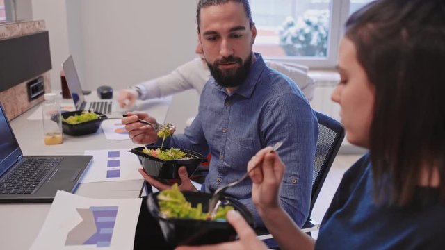Colleagues eating salad and talking seriously at the office desk