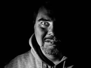 Portrait of bearded adult caucasian man. He smiles like maniac and seems like madness. Black and white shot, low-key lighting. Isolated on black.