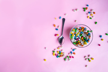 colorful candy in clear wrappers piled in a glass vase isolated on pink background